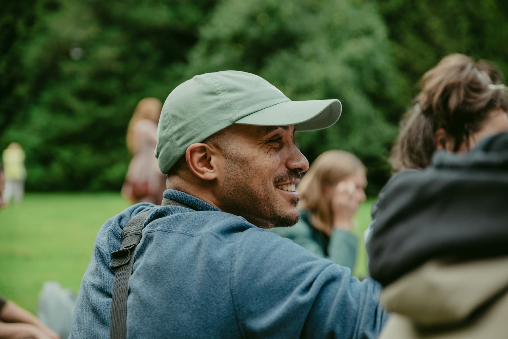Yves im Profil mit Cap, lachend im Grünen